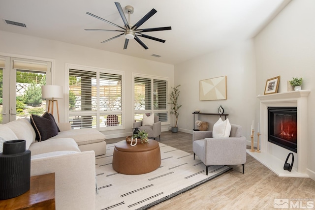 living area featuring a glass covered fireplace, wood finished floors, visible vents, and baseboards