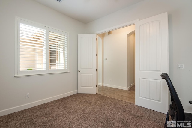 unfurnished bedroom featuring baseboards, arched walkways, and carpet flooring