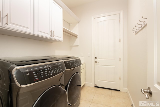 clothes washing area with light tile patterned floors, independent washer and dryer, cabinet space, and baseboards