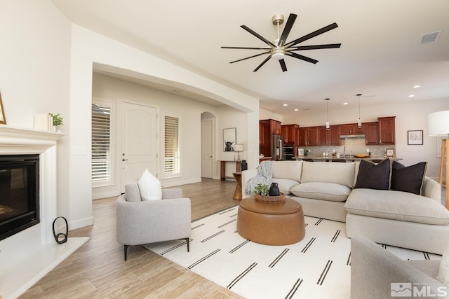 living area featuring light wood finished floors, visible vents, recessed lighting, arched walkways, and a glass covered fireplace