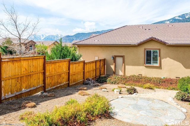 view of property exterior with stucco siding, a mountain view, a tile roof, and fence