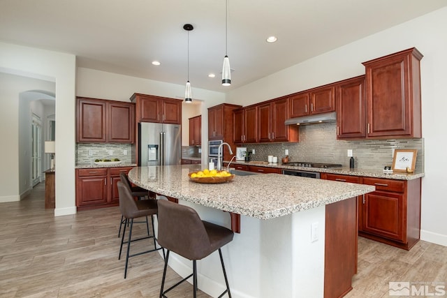 kitchen with light wood-style flooring, arched walkways, a sink, under cabinet range hood, and appliances with stainless steel finishes