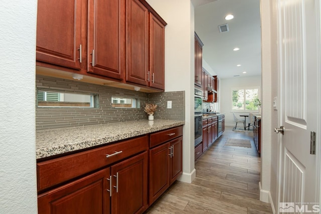 kitchen featuring light stone counters, visible vents, light wood finished floors, recessed lighting, and decorative backsplash