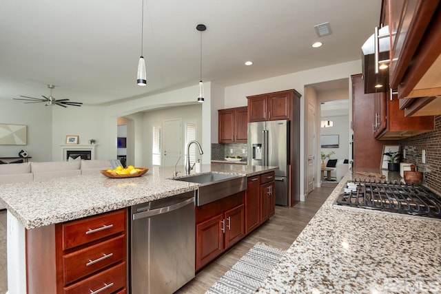 kitchen featuring light stone counters, a fireplace, a sink, appliances with stainless steel finishes, and backsplash