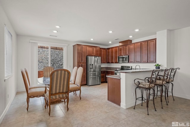 kitchen with recessed lighting, stainless steel appliances, a peninsula, a breakfast bar area, and baseboards