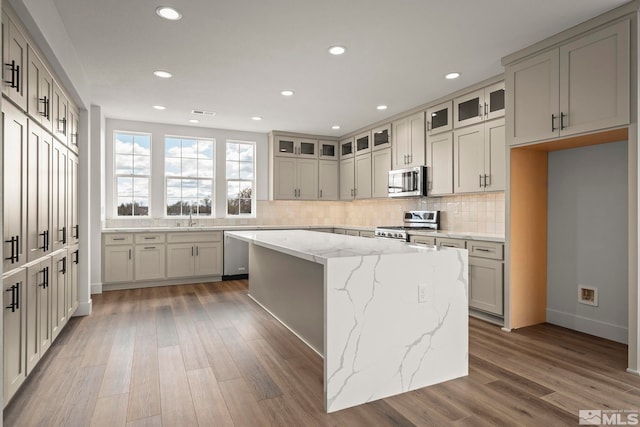 kitchen featuring backsplash, a kitchen island, wood finished floors, appliances with stainless steel finishes, and glass insert cabinets