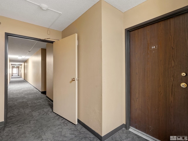 hall featuring baseboards, a textured ceiling, and dark carpet