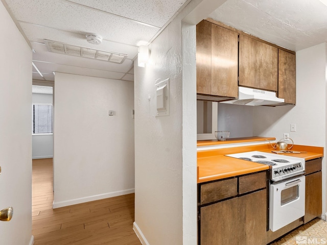 kitchen with baseboards, under cabinet range hood, light countertops, light wood-style floors, and white electric stove