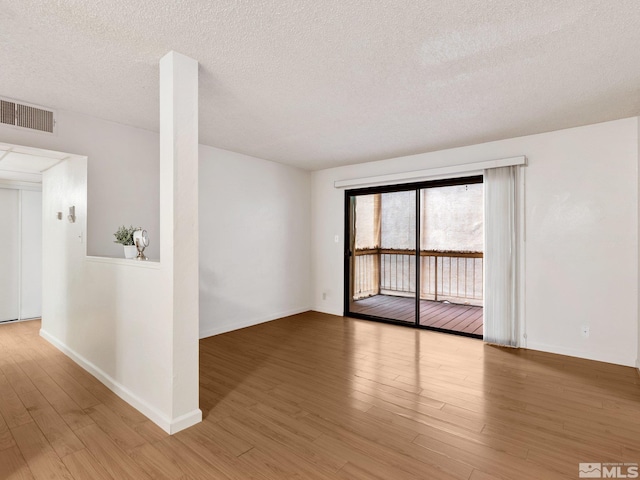 empty room with visible vents, a textured ceiling, baseboards, and wood finished floors