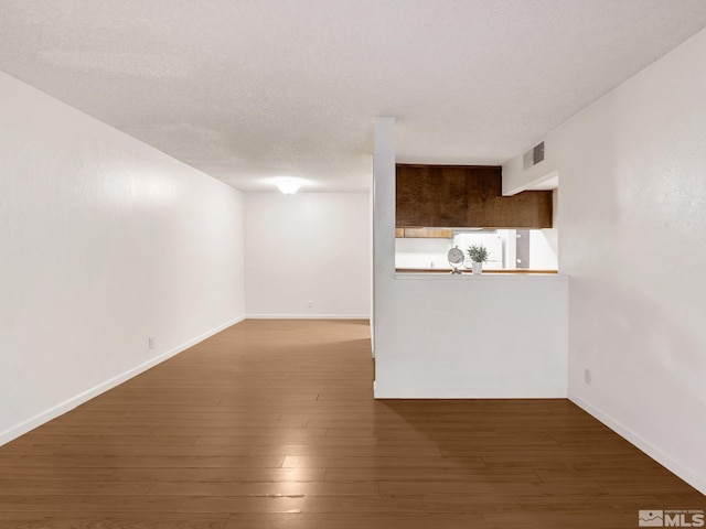 unfurnished living room featuring baseboards, wood finished floors, visible vents, and a textured ceiling