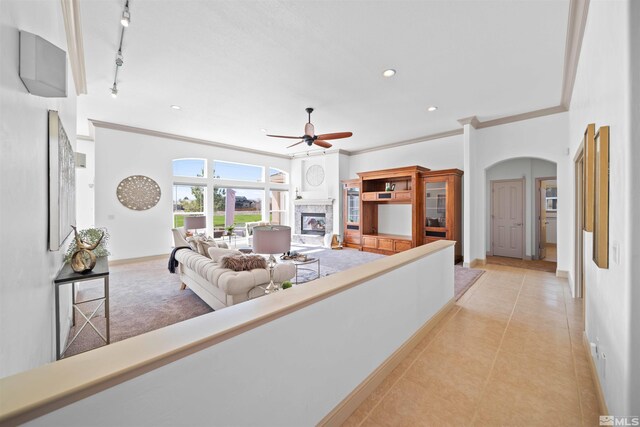 living room with track lighting, light tile patterned flooring, arched walkways, a glass covered fireplace, and a ceiling fan