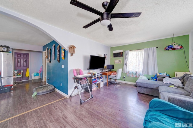 living area featuring baseboards, wood finished floors, arched walkways, a textured ceiling, and a ceiling fan