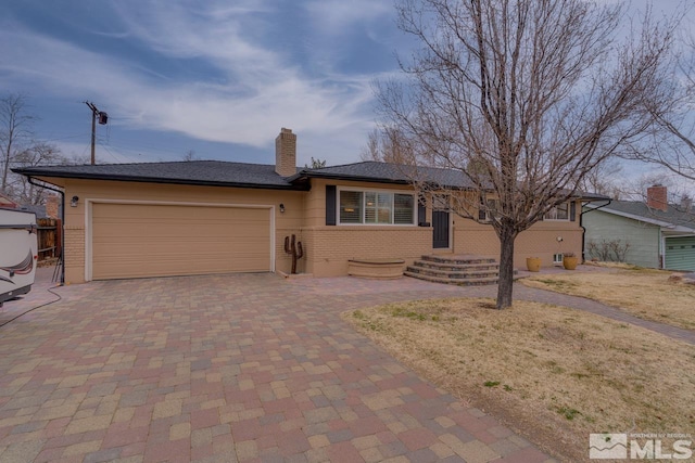 ranch-style home with decorative driveway, brick siding, an attached garage, and a chimney