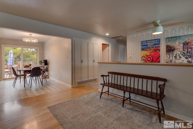 interior space with ceiling fan with notable chandelier, visible vents, wood finished floors, and baseboards