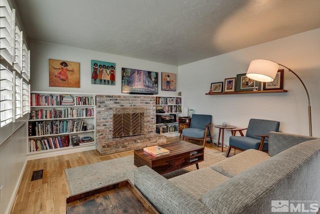 living area featuring visible vents, a fireplace, baseboards, and wood finished floors