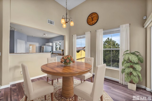 dining room featuring visible vents, high vaulted ceiling, wood finished floors, baseboards, and a chandelier