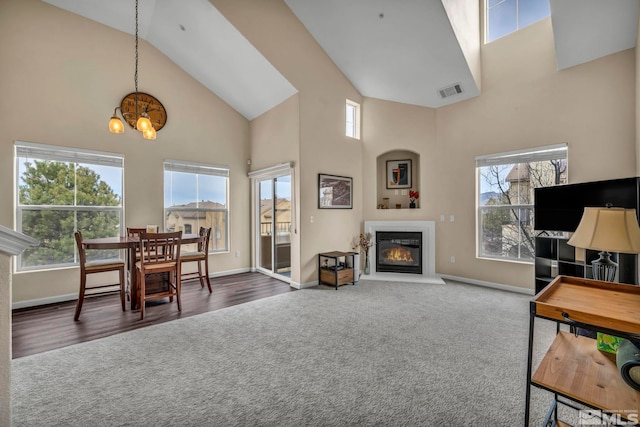 carpeted dining room featuring a glass covered fireplace, plenty of natural light, visible vents, and high vaulted ceiling