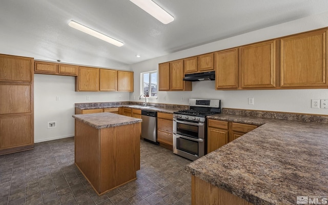 kitchen featuring dark countertops, a kitchen island, under cabinet range hood, stainless steel appliances, and a sink