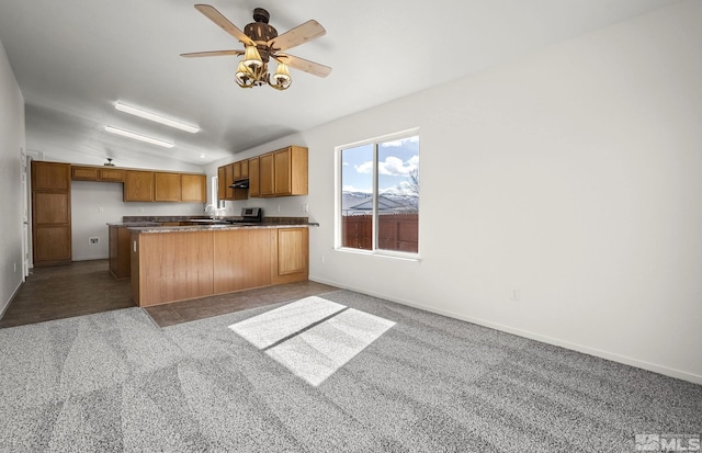 kitchen with a ceiling fan, carpet floors, a peninsula, brown cabinetry, and vaulted ceiling