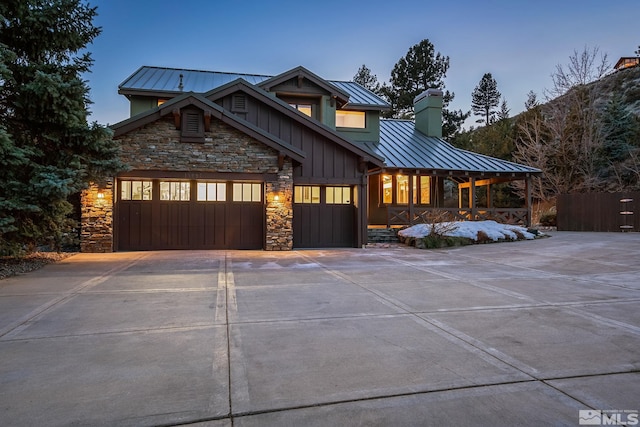 view of front of home featuring board and batten siding, concrete driveway, metal roof, stone siding, and a standing seam roof