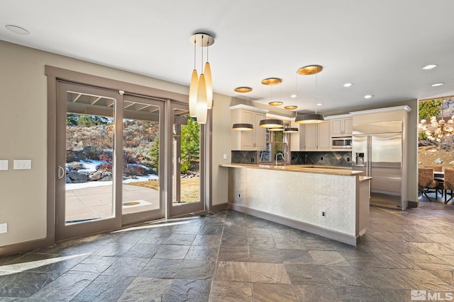 kitchen featuring baseboards, a peninsula, stainless steel appliances, decorative backsplash, and stone tile flooring