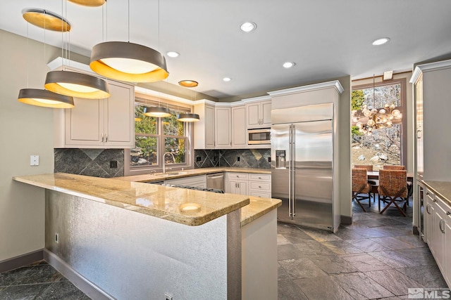 kitchen featuring tasteful backsplash, baseboards, built in appliances, a peninsula, and a sink