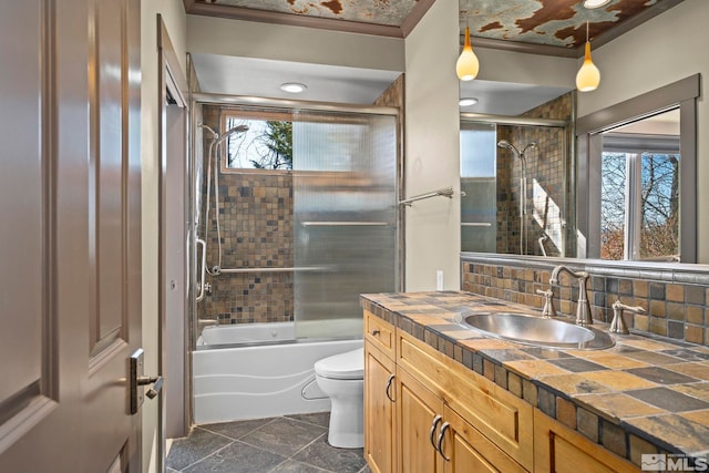 bathroom featuring vanity, decorative backsplash, toilet, and shower / bath combination with glass door