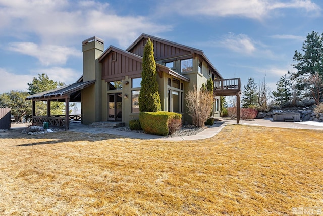 exterior space with a chimney, board and batten siding, a front lawn, and a hot tub