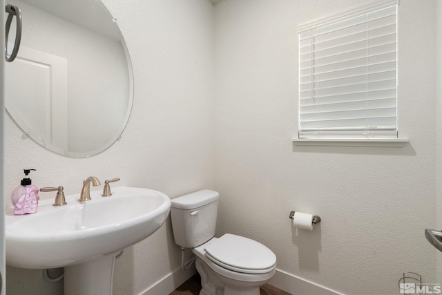 bathroom featuring a sink, toilet, and a textured wall