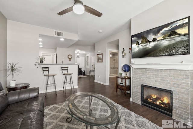 living area with visible vents, a ceiling fan, wood finished floors, baseboards, and a brick fireplace