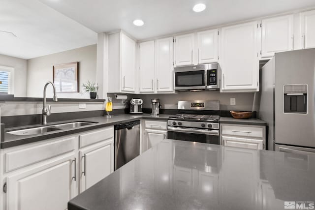 kitchen featuring dark countertops, white cabinets, appliances with stainless steel finishes, and a sink