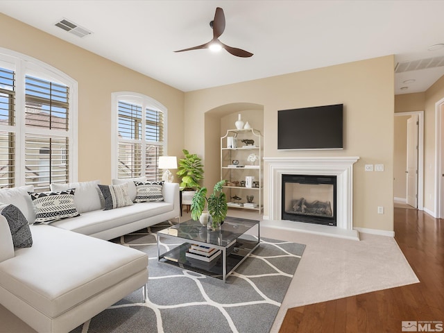 living room with a glass covered fireplace, visible vents, a ceiling fan, and wood finished floors