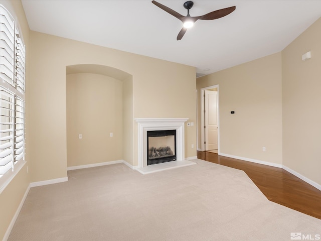 unfurnished living room with wood finished floors, baseboards, a fireplace with raised hearth, and a ceiling fan