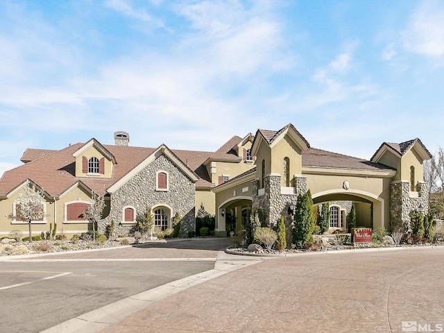 view of front facade featuring a chimney, stone siding, and stucco siding