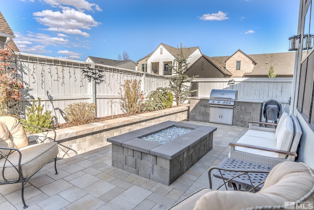 view of patio featuring grilling area, an outdoor kitchen, an outdoor living space with a fire pit, and a fenced backyard