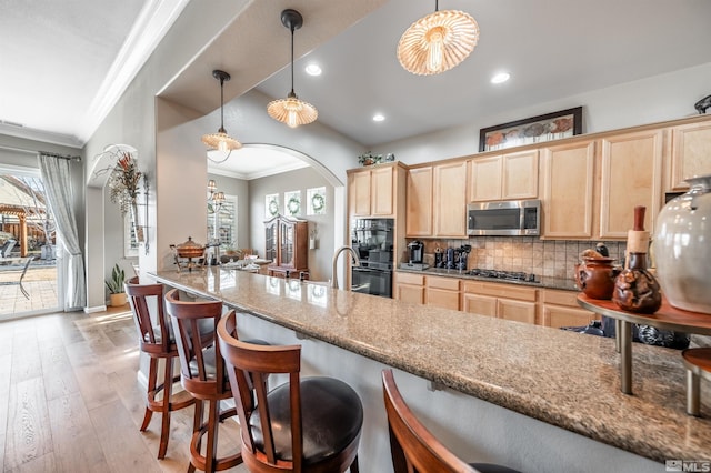 kitchen with light wood finished floors, tasteful backsplash, crown molding, light brown cabinetry, and appliances with stainless steel finishes