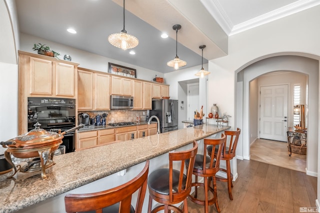 kitchen with light brown cabinets, tasteful backsplash, arched walkways, appliances with stainless steel finishes, and a breakfast bar area