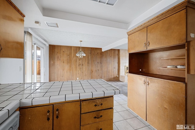 kitchen with tile countertops, brown cabinets, wood walls, and light tile patterned floors