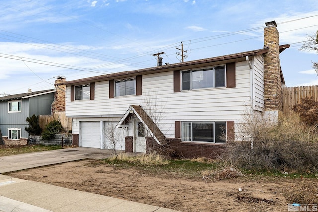 split foyer home with fence, driveway, an attached garage, a chimney, and brick siding