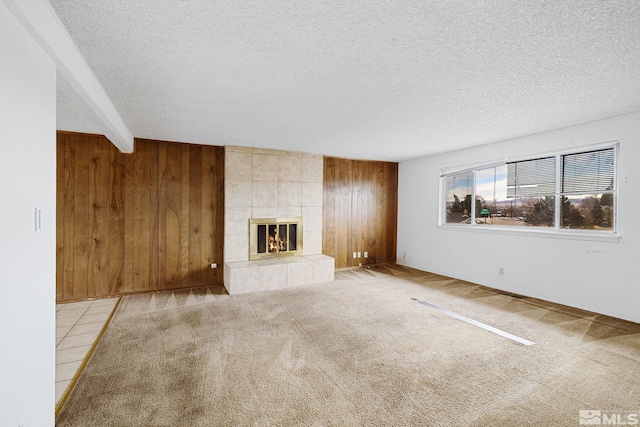 unfurnished living room with a tiled fireplace, carpet flooring, wood walls, and a textured ceiling