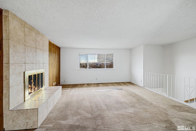 unfurnished living room with a tiled fireplace, carpet flooring, and a textured ceiling