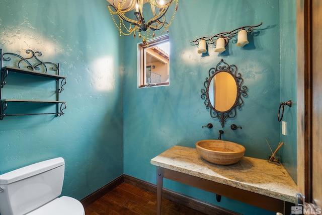 half bathroom with a chandelier, baseboards, toilet, and wood finished floors