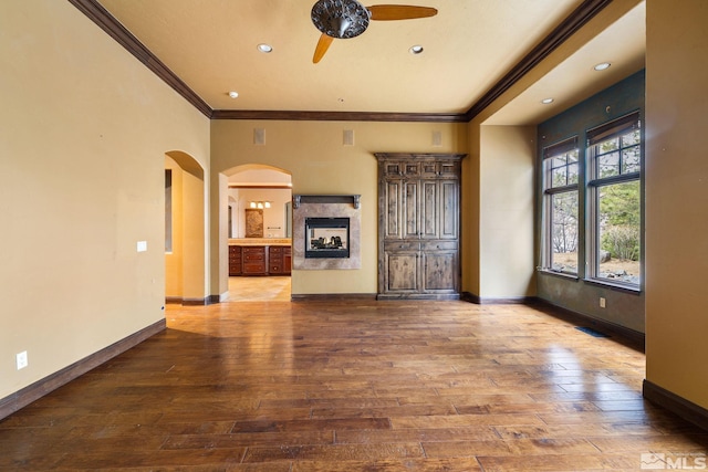 unfurnished living room with baseboards, arched walkways, wood-type flooring, and a ceiling fan