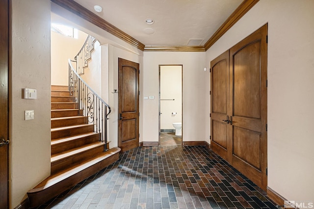 foyer entrance with stairs, crown molding, baseboards, and brick floor