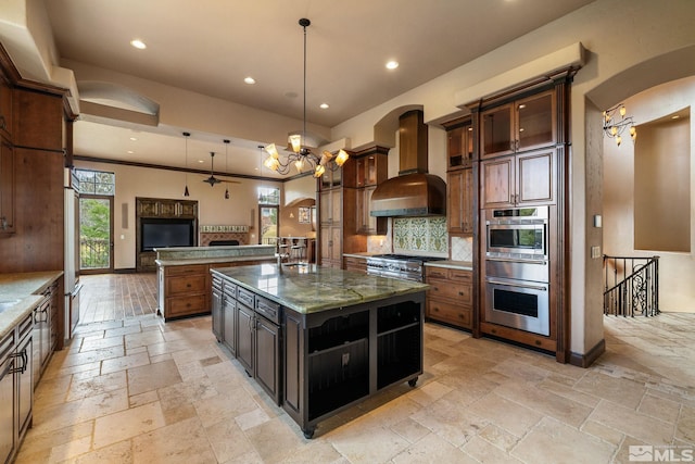 kitchen featuring stone tile floors, a notable chandelier, arched walkways, and wall chimney range hood