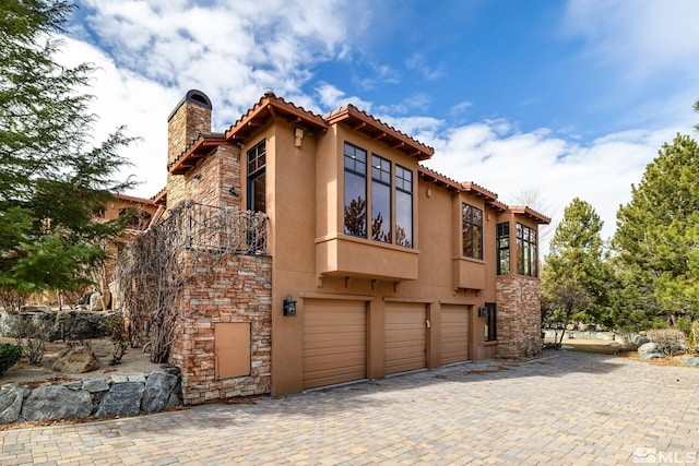 view of front facade with stucco siding, a chimney, a garage, stone siding, and driveway