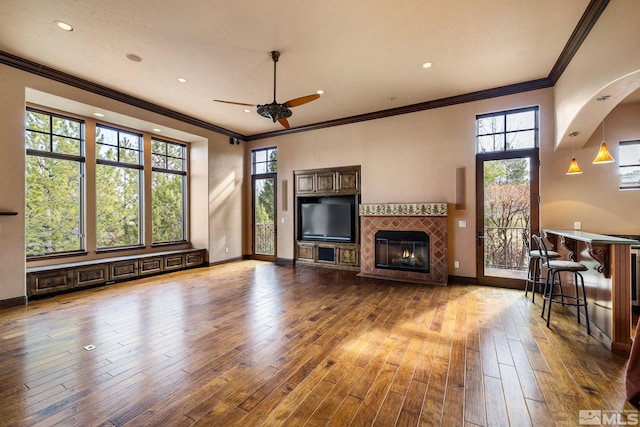 living room featuring ornamental molding, a ceiling fan, wood-type flooring, a fireplace, and baseboards