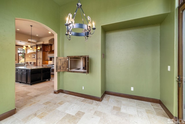 interior space with stone tile floors, a notable chandelier, arched walkways, and baseboards