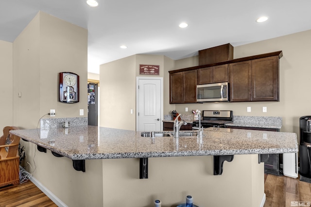 kitchen with light stone countertops, stainless steel appliances, dark wood-type flooring, and a sink