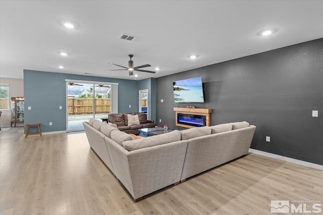 living area featuring a wealth of natural light, visible vents, light wood-style floors, and a glass covered fireplace